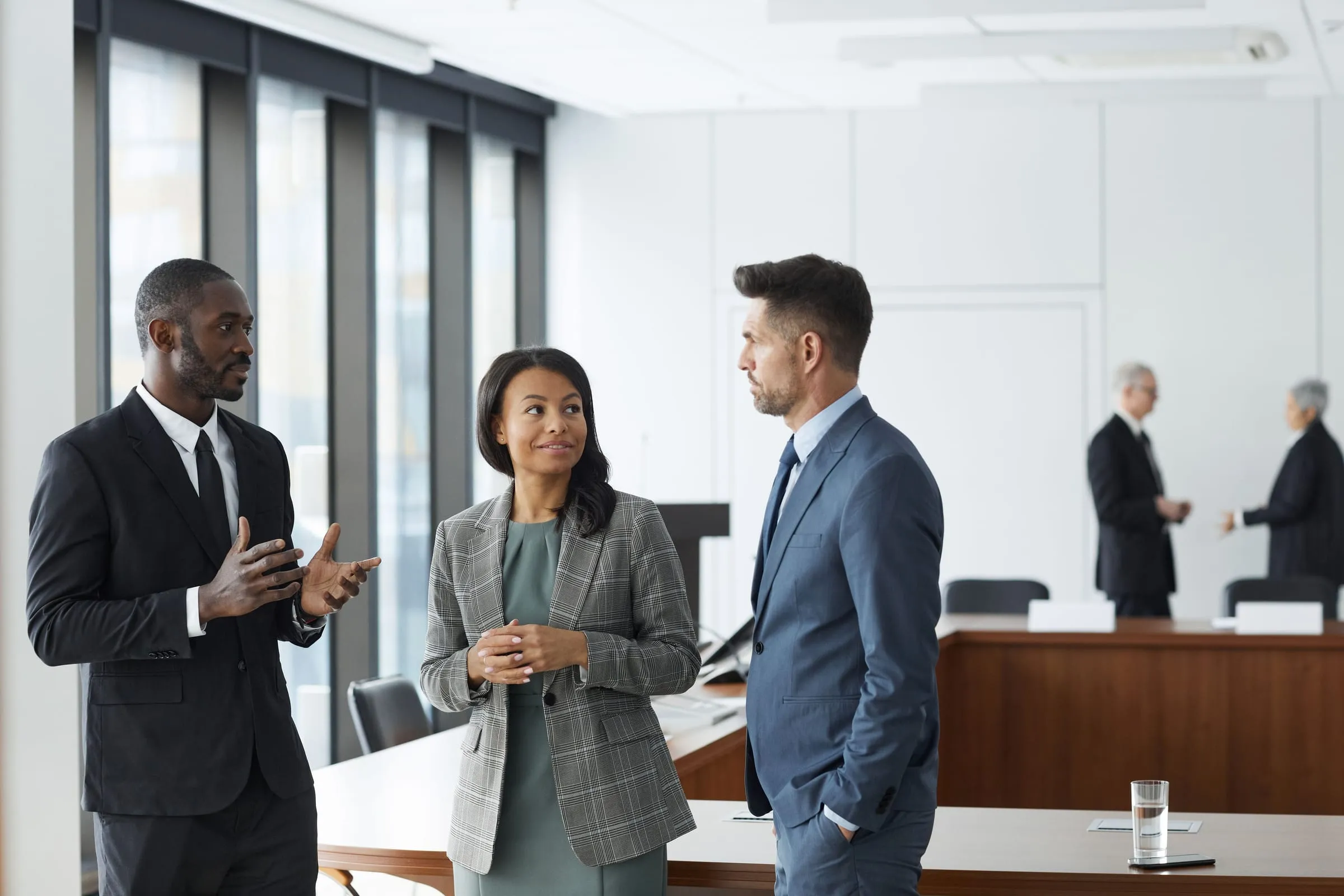 Three business professionals talking together in a bright modern boardroom